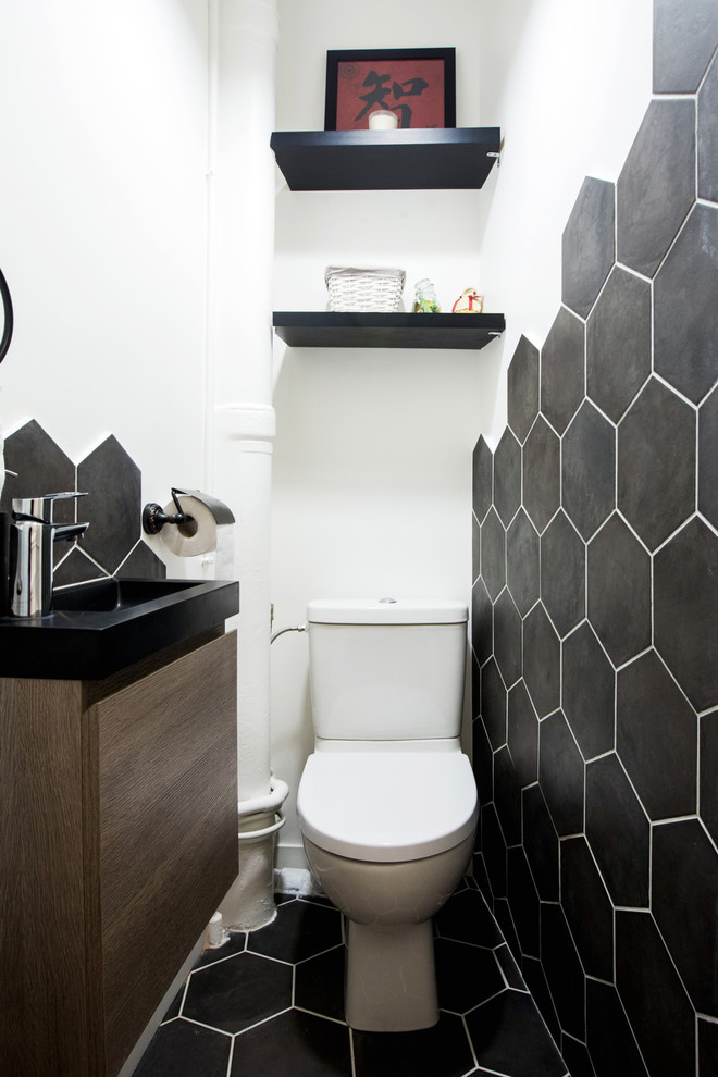 パリにある小さなトランジショナルスタイルのおしゃれなトイレ・洗面所 (中間色木目調キャビネット、一体型トイレ	、黒いタイル、セラミックタイル、白い壁、セラミックタイルの床、壁付け型シンク、御影石の洗面台、黒い床、黒い洗面カウンター) の写真