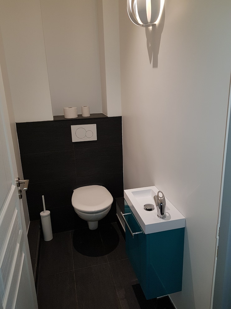 Cette image montre un petit WC suspendu design avec un placard à porte plane, des portes de placard turquoises, un carrelage noir, des carreaux de céramique, un mur blanc, un sol en carrelage de céramique, un lavabo suspendu, un plan de toilette en carrelage et un sol noir.