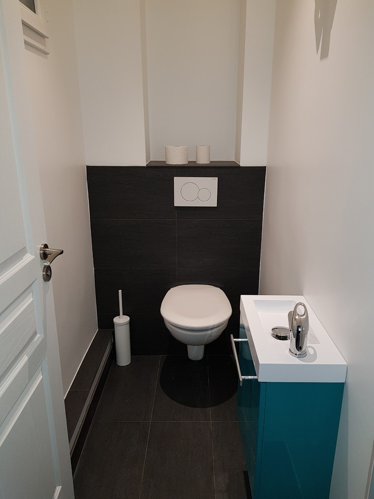 Modern inredning av ett litet toalett, med släta luckor, turkosa skåp, en vägghängd toalettstol, svart kakel, keramikplattor, vita väggar, klinkergolv i keramik, ett väggmonterat handfat, kaklad bänkskiva och svart golv