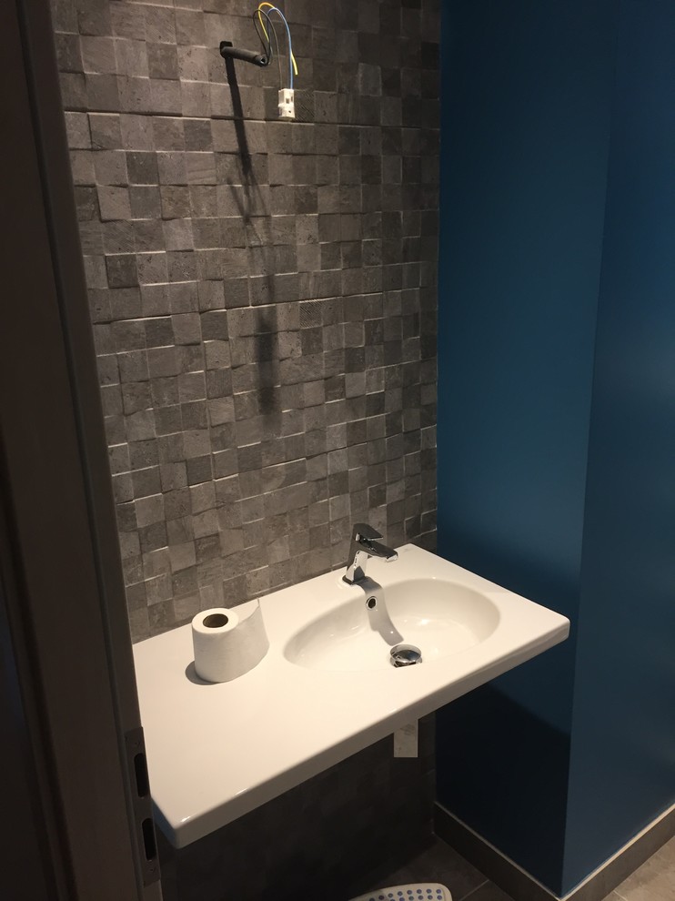Cette image montre un WC suspendu design de taille moyenne avec un carrelage gris, des carreaux de céramique, un mur gris, un sol en carrelage de céramique et un lavabo intégré.