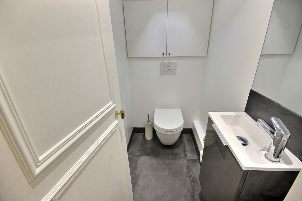 Small modern cloakroom in Paris with grey cabinets, a wall mounted toilet, grey tiles, cement tiles, white walls, cement flooring, a wall-mounted sink, solid surface worktops, grey floors, white worktops, a floating vanity unit and exposed beams.