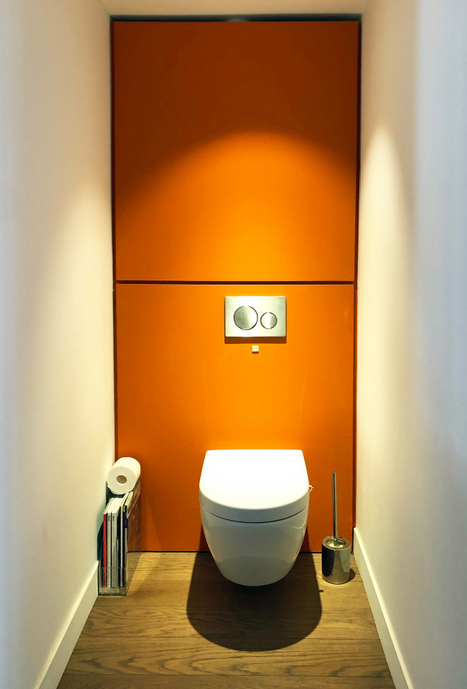 Foto di un bagno di servizio design di medie dimensioni con WC sospeso, pareti arancioni, parquet scuro e pavimento marrone