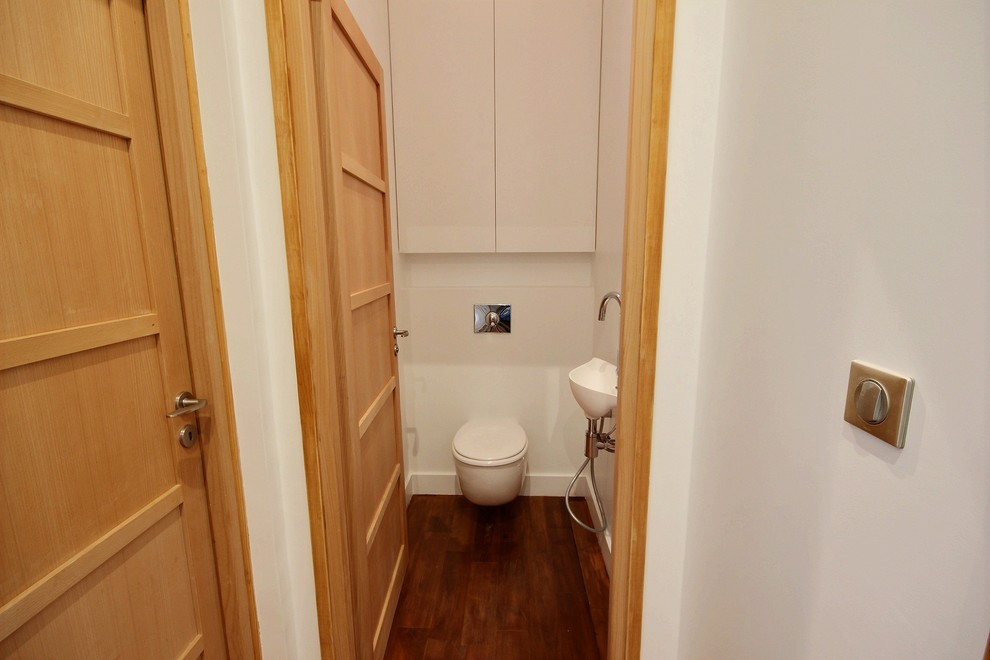 Small industrial cloakroom in Paris with white cabinets, a wall mounted toilet, white walls, medium hardwood flooring and a wall-mounted sink.