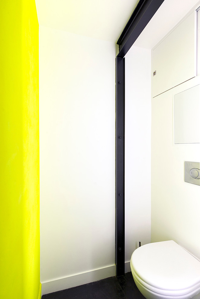 Idée de décoration pour un petit WC suspendu design avec un placard à porte affleurante, des portes de placard blanches, un mur jaune, sol en béton ciré, un sol noir, meuble-lavabo encastré et un plafond décaissé.