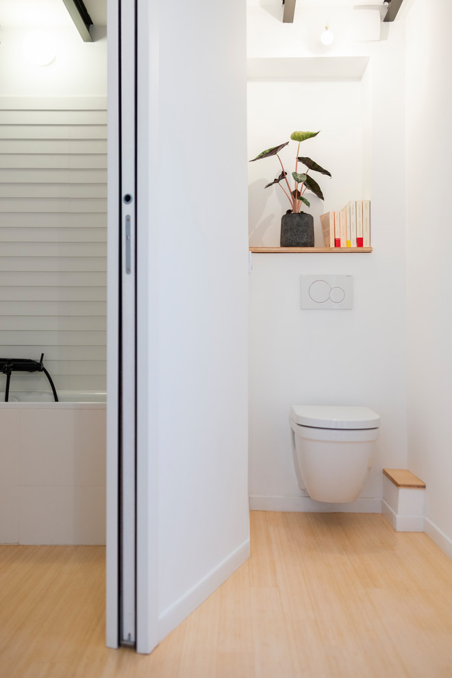 Cette image montre un WC suspendu design avec un placard avec porte à panneau encastré, un mur blanc, parquet en bambou et un plan de toilette en bois.