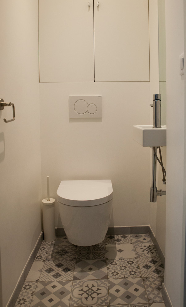 Kleine Moderne Gästetoilette mit Kassettenfronten, weißen Schränken, Wandtoilette, weißer Wandfarbe, Zementfliesen für Boden, Wandwaschbecken und buntem Boden in Paris