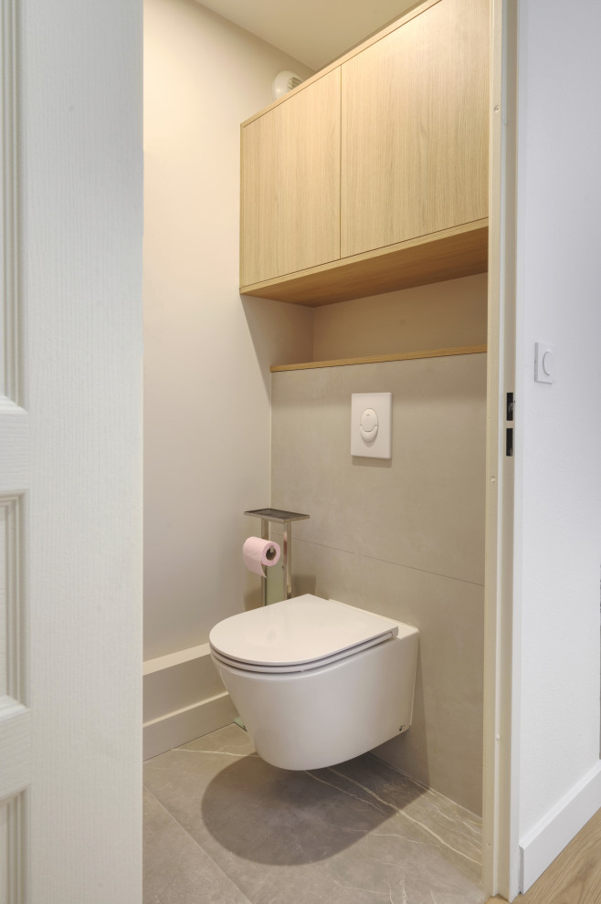 Immagine di un bagno di servizio moderno di medie dimensioni con ante a filo, ante in legno chiaro, WC sospeso, piastrelle beige, pareti beige, pavimento grigio e mobile bagno sospeso