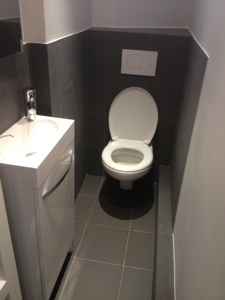 Exempel på ett litet modernt vit vitt toalett, med luckor med profilerade fronter, vita skåp, en vägghängd toalettstol, grå kakel, keramikplattor, vita väggar, klinkergolv i keramik, ett väggmonterat handfat och grått golv