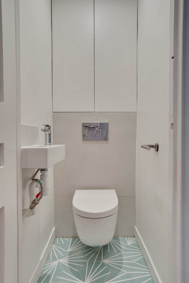 Modern inredning av ett litet toalett, med luckor med profilerade fronter, vita skåp, en vägghängd toalettstol, grå kakel, cementkakel, grönt golv, grå väggar och cementgolv