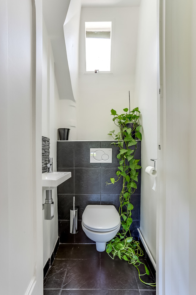 パリにある高級な中くらいなコンテンポラリースタイルのおしゃれなトイレ・洗面所 (壁付け型シンク、壁掛け式トイレ、黒いタイル、白い壁) の写真