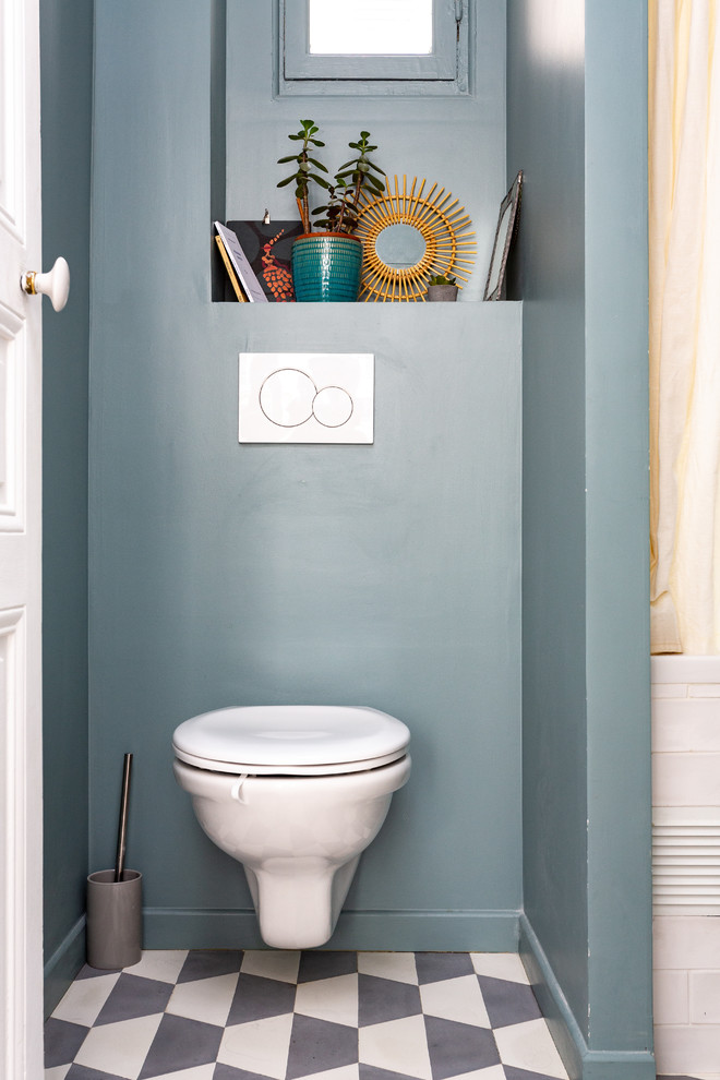 Nordisk inredning av ett litet toalett, med en vägghängd toalettstol, blå väggar, cementgolv och flerfärgat golv