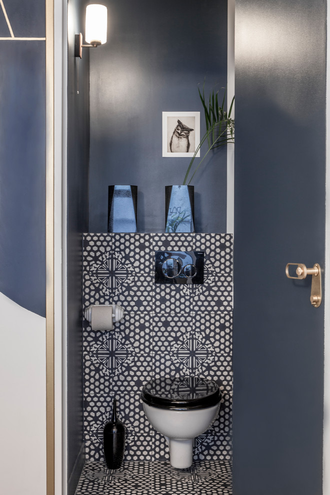 Cette image montre un petit WC suspendu design avec un placard à porte affleurante, des portes de placard bleues, un carrelage multicolore, des carreaux de béton, un mur bleu, carreaux de ciment au sol, un lavabo intégré, un plan de toilette en surface solide et un sol multicolore.
