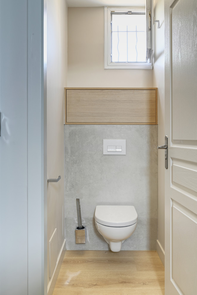 Exemple d'un WC suspendu chic en bois clair de taille moyenne avec un placard à porte affleurante, un carrelage beige, un carrelage de pierre, un mur beige, sol en stratifié et un sol beige.