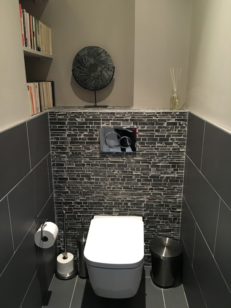 Aménagement d'un petit WC suspendu contemporain avec un placard sans porte, un mur blanc, carreaux de ciment au sol, un plan de toilette en carrelage et un sol gris.