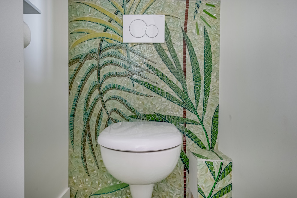 Modelo de aseo tropical con puertas de armario verdes, sanitario de pared, baldosas y/o azulejos verdes, baldosas y/o azulejos en mosaico, suelo con mosaicos de baldosas, encimera de madera y suelo verde