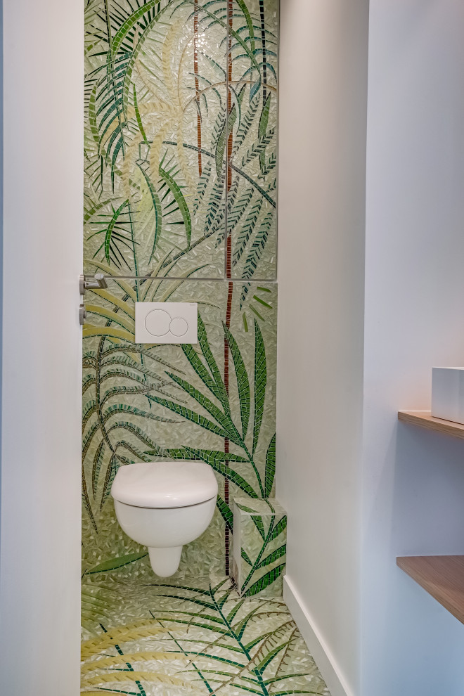 Idee per un bagno di servizio tropicale con ante verdi, WC sospeso, piastrelle verdi, piastrelle a mosaico, pavimento con piastrelle a mosaico, top in legno e pavimento verde