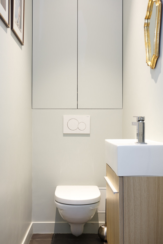 Inspiration för små vitt toaletter, med luckor med profilerade fronter, vita skåp, en vägghängd toalettstol, vit kakel, vita väggar, klinkergolv i keramik, ett väggmonterat handfat, bänkskiva i akrylsten och grått golv