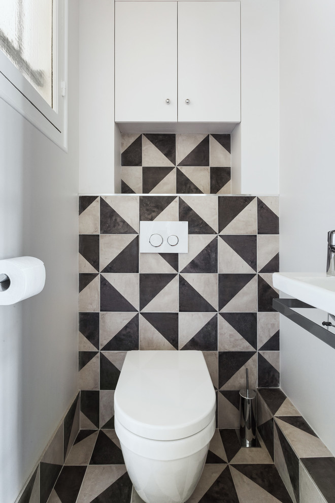 Modern inredning av ett litet toalett, med släta luckor, vita skåp, en vägghängd toalettstol, svart och vit kakel, cementkakel, vita väggar, cementgolv, ett väggmonterat handfat och svart golv