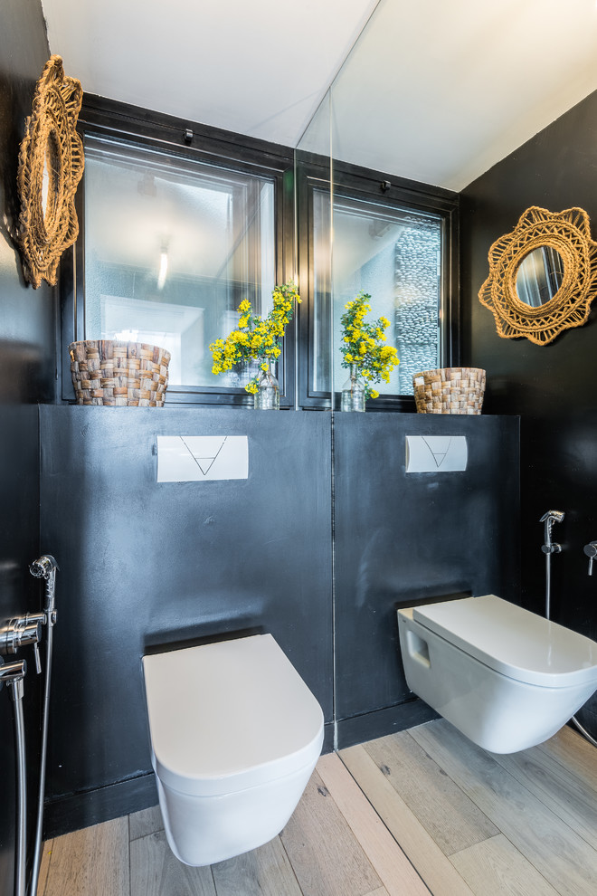 Bild på ett eklektiskt toalett, med en vägghängd toalettstol, svarta väggar, ljust trägolv och beiget golv