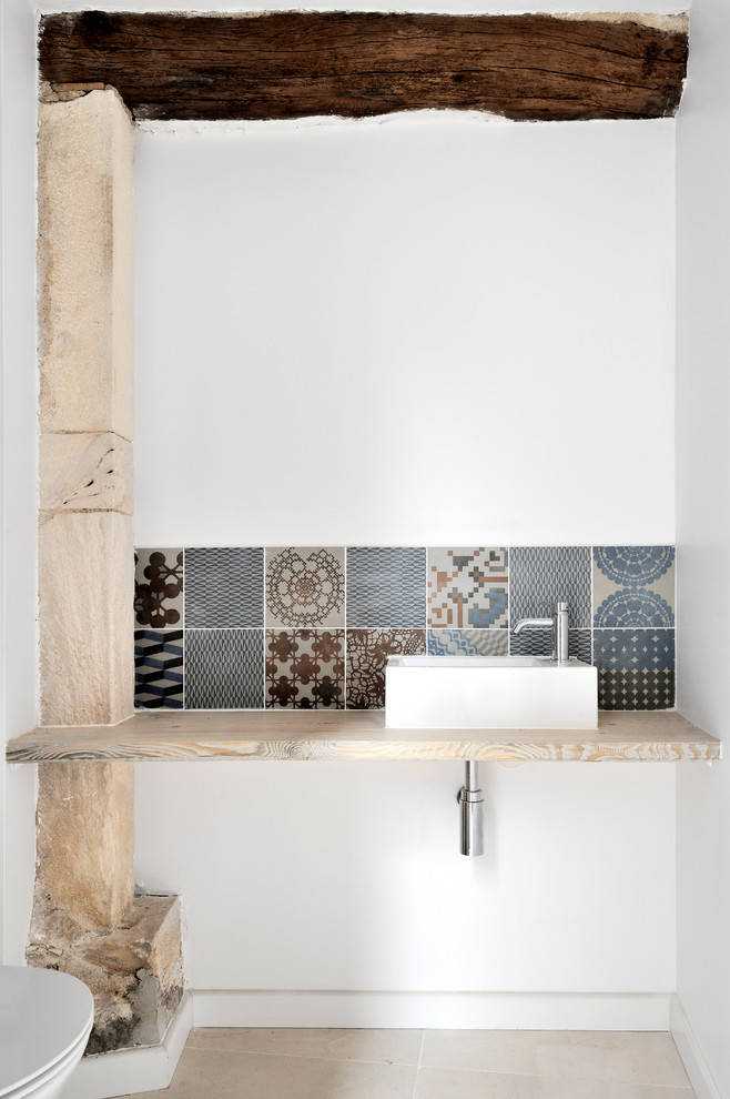 На фото: туалет в средиземноморском стиле с инсталляцией, керамической плиткой, белыми стенами, полом из керамической плитки, столешницей из дерева, разноцветной плиткой и настольной раковиной с