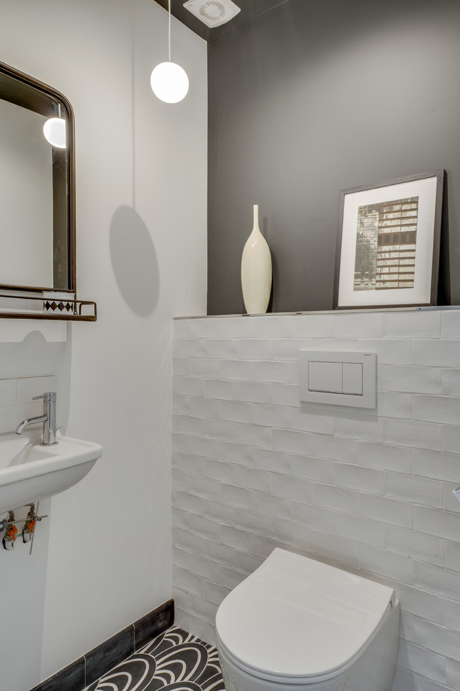 Bild på ett litet lantligt toalett, med en vägghängd toalettstol, vit kakel, perrakottakakel, svarta väggar, cementgolv, ett väggmonterat handfat och svart golv