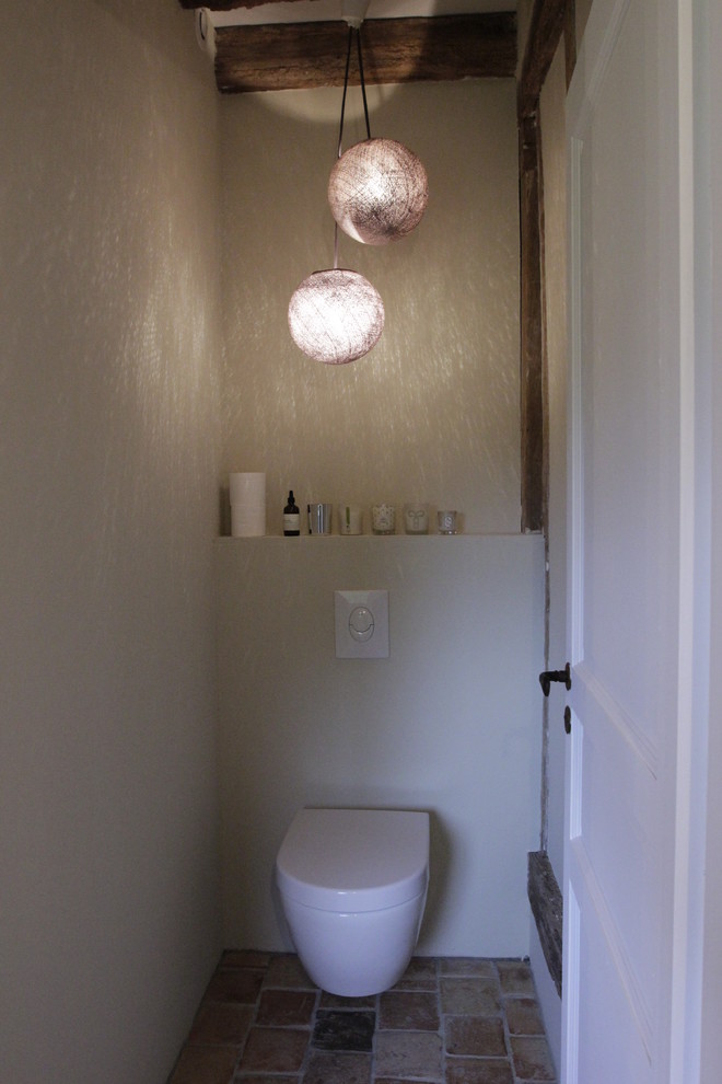 Réalisation d'un petit WC suspendu champêtre avec un mur beige et tomettes au sol.
