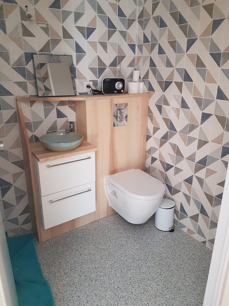 Bild på ett litet skandinaviskt beige beige toalett, med släta luckor, en vägghängd toalettstol, flerfärgad kakel, perrakottakakel, vita väggar, terrazzogolv, ett fristående handfat, träbänkskiva, blått golv och skåp i ljust trä