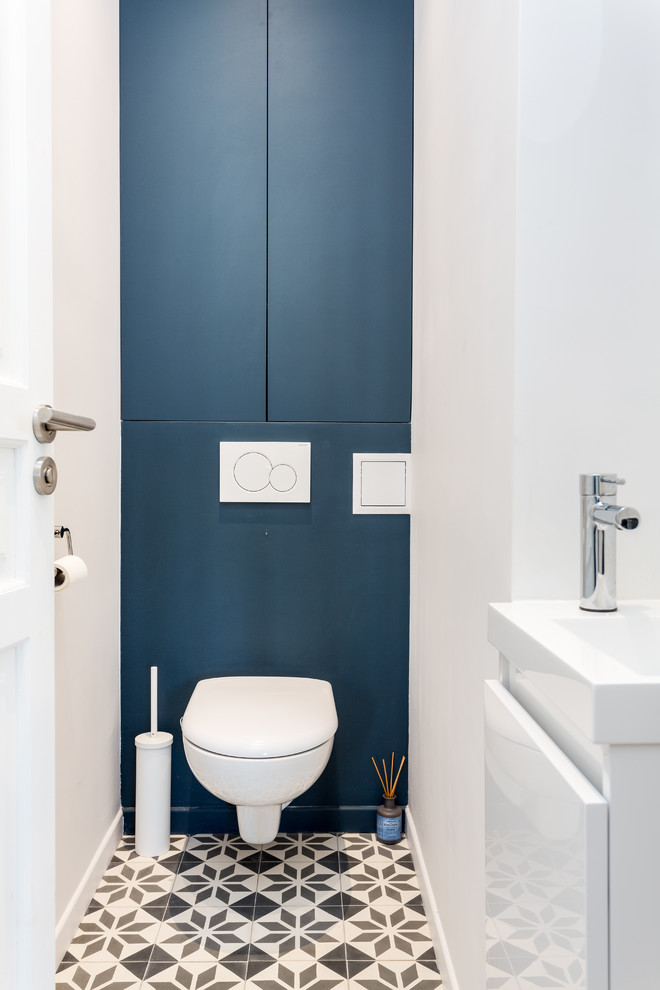 パリにあるお手頃価格の小さなモダンスタイルのおしゃれなトイレ・洗面所 (インセット扉のキャビネット、青いキャビネット、壁掛け式トイレ、白いタイル、青い壁、セメントタイルの床、壁付け型シンク、人工大理石カウンター、グレーの床、白い洗面カウンター) の写真