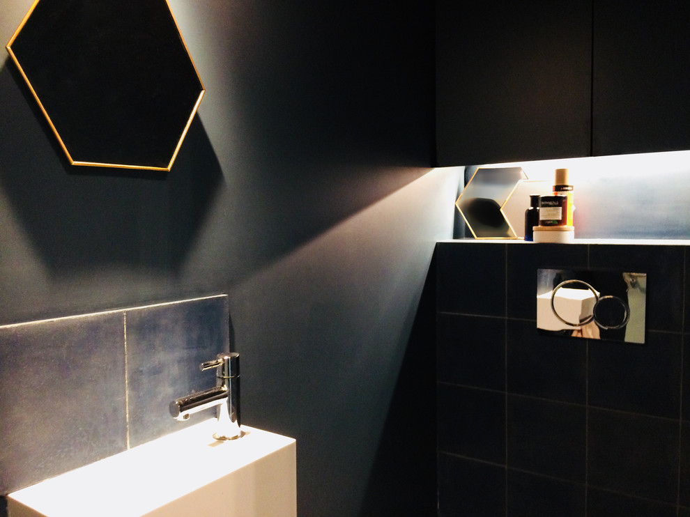 Idée de décoration pour un petit WC suspendu design avec un placard à porte affleurante, des portes de placard noires, un carrelage bleu, des carreaux de béton, un mur bleu, carreaux de ciment au sol, un lavabo suspendu et un sol bleu.