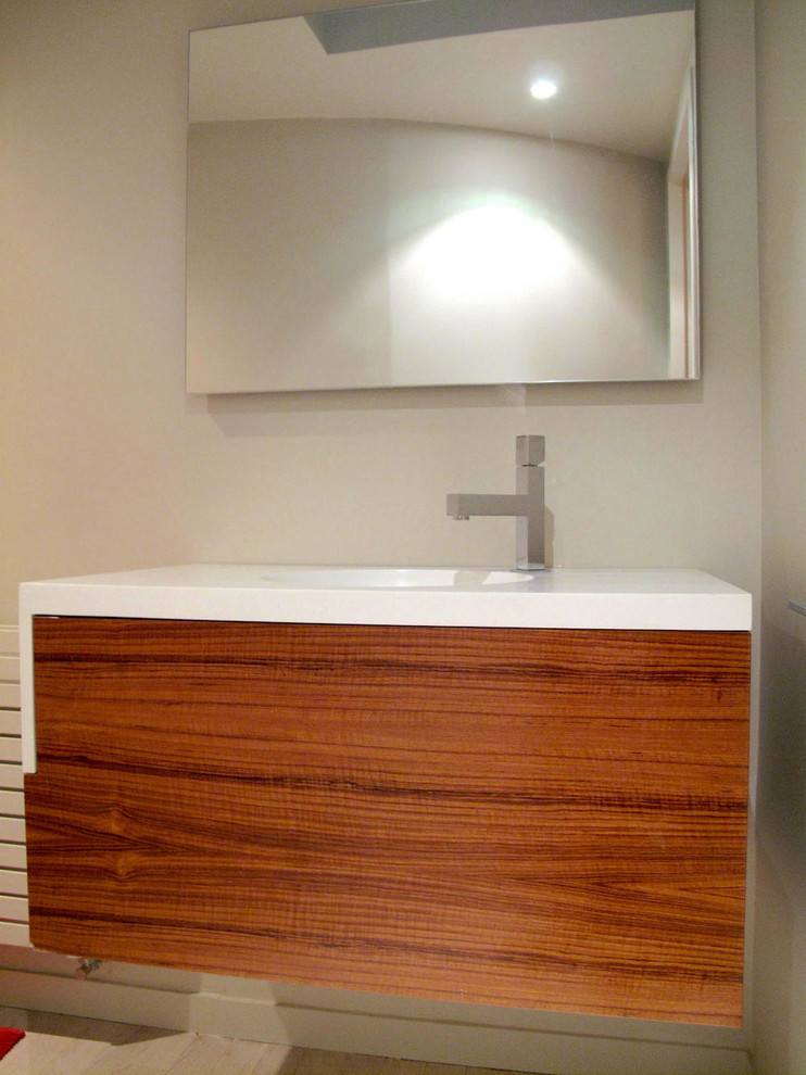 Inspiration for a small modern cloakroom in Paris with flat-panel cabinets, medium wood cabinets, a wall mounted toilet, beige tiles, beige walls, painted wood flooring, an integrated sink, solid surface worktops, beige floors and white worktops.