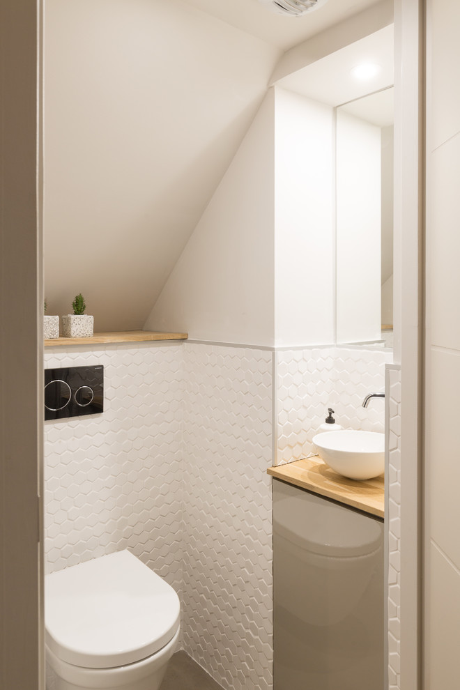 Cette image montre un WC suspendu design de taille moyenne avec un placard à porte affleurante, des portes de placard beiges, un carrelage blanc, des carreaux de céramique, un mur blanc, sol en béton ciré, une vasque, un plan de toilette en bois et un sol gris.