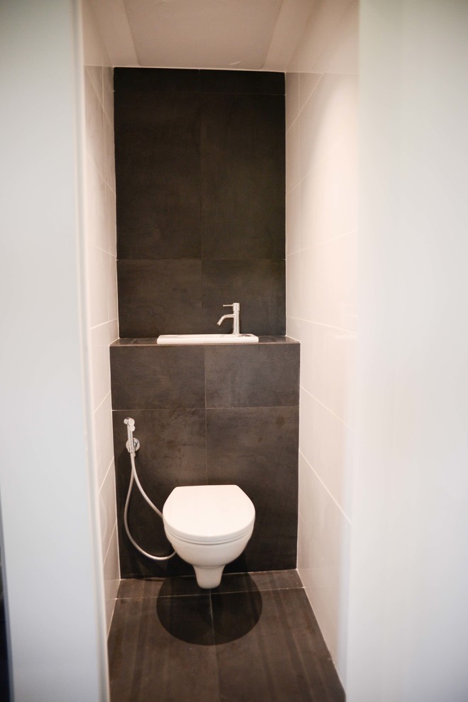 На фото: туалет среднего размера с инсталляцией, черной плиткой, керамической плиткой, белыми стенами, полом из керамической плитки, монолитной раковиной, столешницей из плитки и черным полом