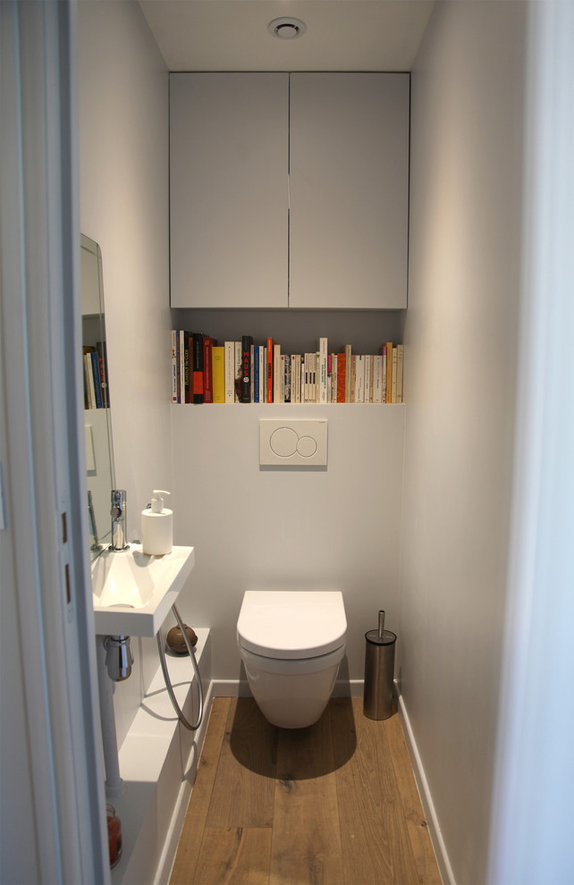 Стильный дизайн: туалет среднего размера в современном стиле с серыми фасадами, инсталляцией, серыми стенами, светлым паркетным полом, подвесной раковиной и открытыми фасадами - последний тренд