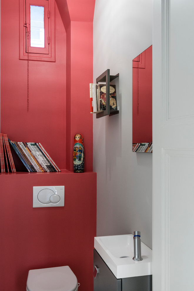 Inredning av ett modernt toalett, med en vägghängd toalettstol, beige kakel, röda väggar, klinkergolv i keramik och ett väggmonterat handfat