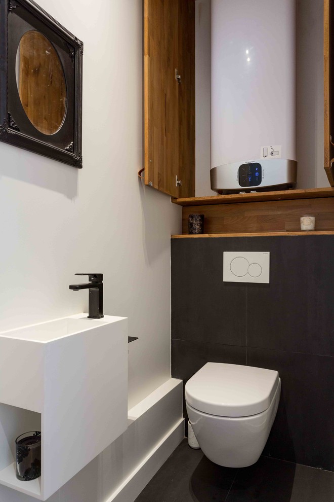 Mid-sized trendy black tile and ceramic tile ceramic tile and black floor powder room photo in Paris with flat-panel cabinets, brown cabinets, a wall-mount toilet, white walls, a vessel sink and white countertops