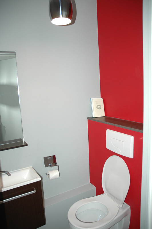 Ejemplo de aseo moderno de tamaño medio con armarios con paneles lisos, puertas de armario negras, sanitario de pared, paredes rojas, lavabo tipo consola y encimera de acrílico