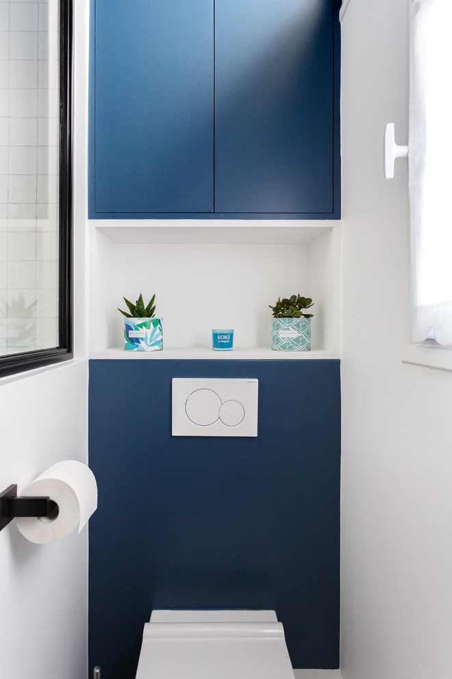 Immagine di un piccolo bagno di servizio moderno con ante a filo, ante blu, WC sospeso, piastrelle bianche, piastrelle in ceramica, pareti blu, pavimento con piastrelle in ceramica, pavimento grigio e top bianco