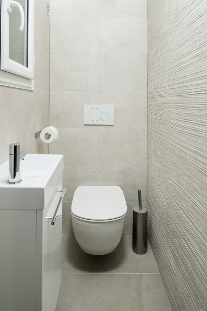Foto på ett litet funkis toalett, med en vägghängd toalettstol, beige kakel, keramikplattor, beige väggar, klinkergolv i keramik, ett väggmonterat handfat, släta luckor, vita skåp och beiget golv