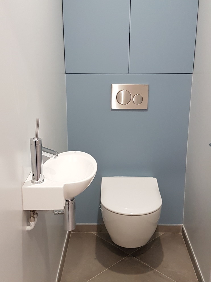 Idée de décoration pour un WC suspendu design avec des portes de placard bleues, un mur blanc, un sol en carrelage de céramique, un lavabo suspendu et un sol gris.