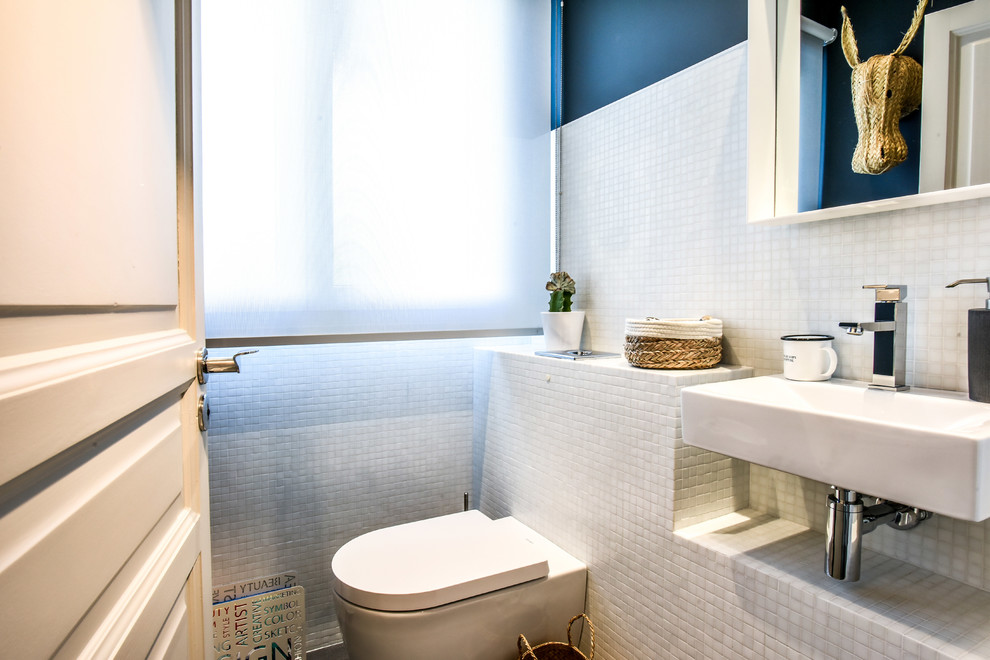 他の地域にあるコンテンポラリースタイルのおしゃれなトイレ・洗面所 (壁掛け式トイレ、白いタイル、モザイクタイル、青い壁、壁付け型シンク) の写真