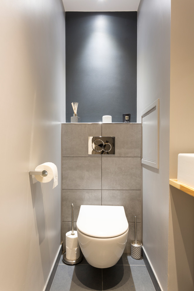 Cette image montre un grand WC suspendu minimaliste avec un placard à porte plane, des portes de placard blanches, un carrelage gris, un mur gris, une vasque, un plan de toilette en bois, un sol gris, des carreaux de porcelaine, un sol en carrelage de porcelaine et un plan de toilette marron.