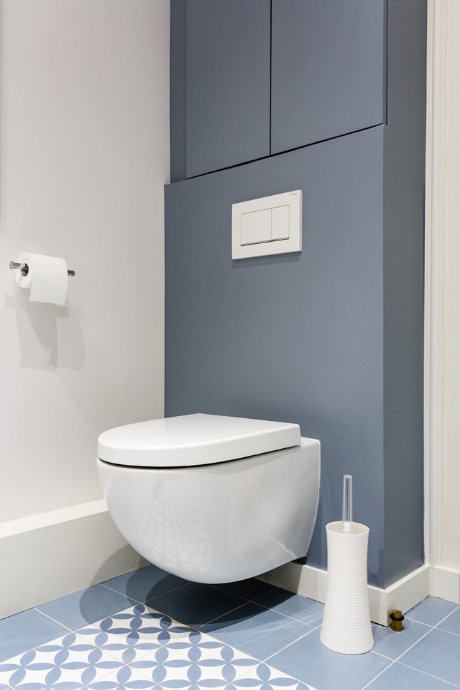 Cette photo montre un petit WC suspendu moderne avec un placard à porte affleurante, des portes de placard grises, un mur gris, carreaux de ciment au sol, un sol gris et un plan de toilette blanc.
