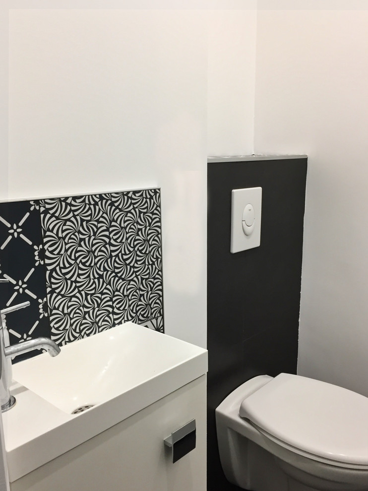 Foto på ett mellanstort funkis svart toalett, med en vägghängd toalettstol, vita väggar, klinkergolv i keramik, ett avlångt handfat, svart golv, släta luckor, skåp i ljust trä, cementkakel och granitbänkskiva