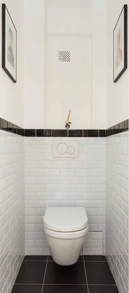 Cette image montre un petit WC suspendu minimaliste avec un carrelage blanc, un mur blanc, un sol en carrelage de céramique, un sol noir, un plan de toilette blanc, des portes de placard blanches et un carrelage métro.