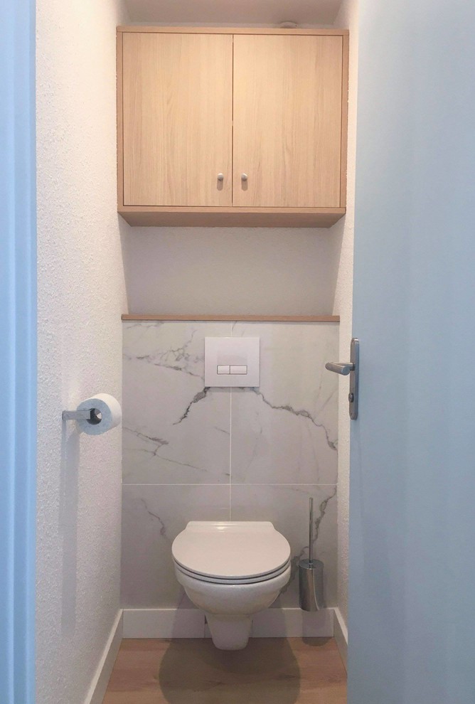 Idéer för att renovera ett mellanstort maritimt brun brunt toalett, med luckor med infälld panel, bruna skåp, en vägghängd toalettstol, vit kakel, marmorkakel, vita väggar, laminatgolv, laminatbänkskiva och brunt golv