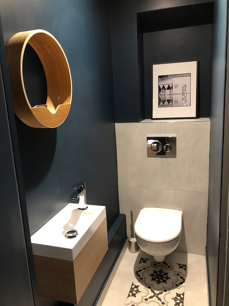 Small contemporary cloakroom in Paris with a wall mounted toilet, grey tiles, ceramic tiles, blue walls, cement flooring, a console sink, solid surface worktops, grey floors and white worktops.