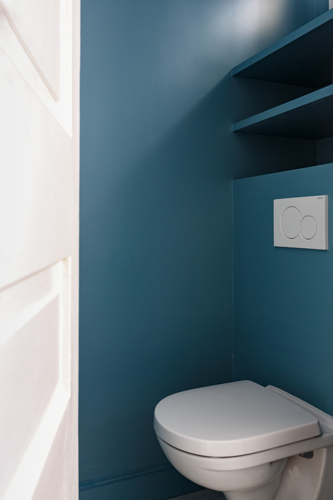Kleine Moderne Gästetoilette mit offenen Schränken, blauen Schränken, Wandtoilette, blauen Fliesen, blauer Wandfarbe und weißer Waschtischplatte in Paris