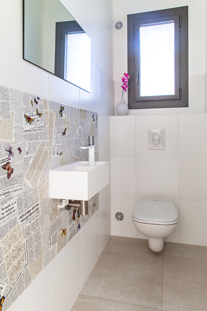 На фото: туалет среднего размера в современном стиле с биде, белой плиткой, керамической плиткой, бежевыми стенами, полом из цементной плитки, раковиной с несколькими смесителями, столешницей из искусственного камня и бежевым полом с