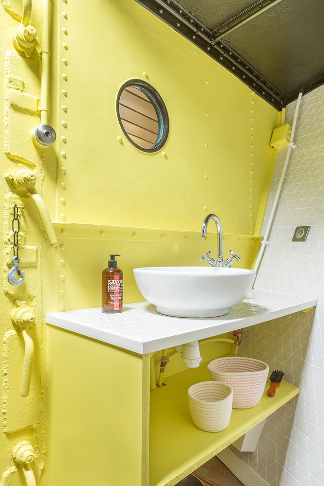 Maritim inredning av ett toalett, med öppna hyllor, gula skåp, gula väggar och ett fristående handfat