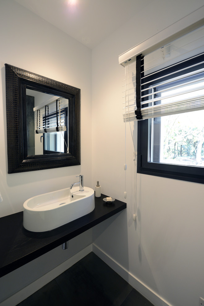 Foto di un piccolo bagno di servizio minimal con WC sospeso, pareti bianche, pavimento con piastrelle in ceramica, lavabo da incasso, top in superficie solida, pavimento grigio e top nero